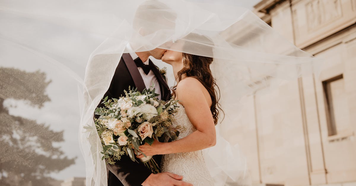 Bride and groom share a tender kiss under a veil, showcasing love and romance on their special day.