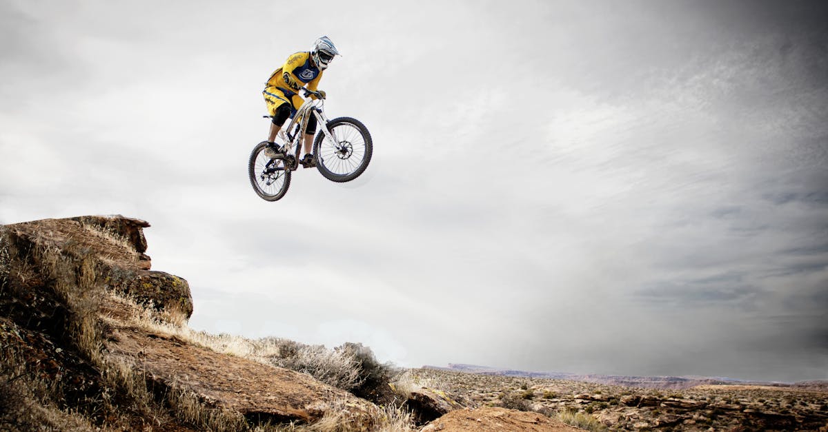 A cyclist performs a daring jump off a rocky cliff under a cloudy sky.